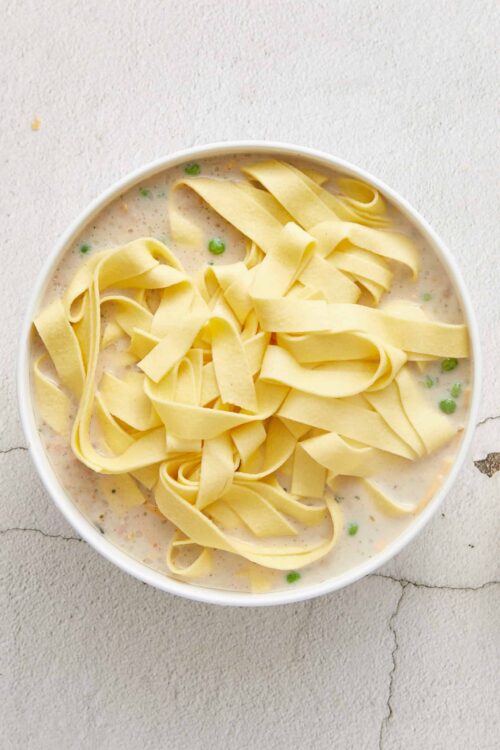 Creamy chicken and vegetable pasta soup with fettuccine and peas in a white bowl.