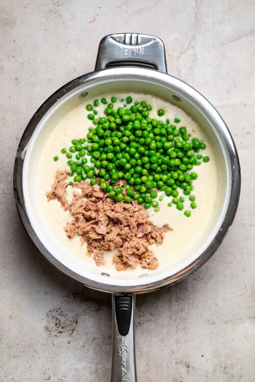 Fresh green peas and canned tuna in a creamy white sauce in a stainless steel saucepan.