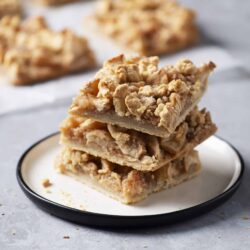 Butterscotch Apple Butter Bars with Oat Crumble on a black-rimmed white plate, fresh-out-of-the-oven treat for dessert or snack.