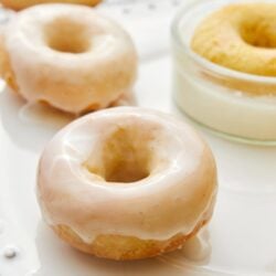 Fluffy vanilla-glazed donuts on a white plate with a small bowl of glaze.