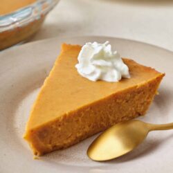 Creamy pumpkin pie with whipped cream on a beige plate for fall dessert.