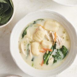 Creamy chicken and gnocchi soup with spinach and carrots, served in a white bowl for comforting homemade meal.