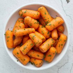 Golden glazed carrots garnished with fresh herbs in a white bowl.