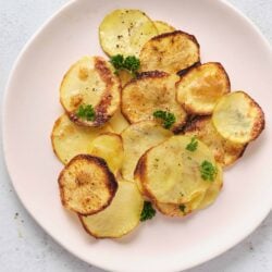 Thinly sliced roasted potatoes garnished with parsley on a white plate.