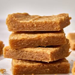 Butterscotch blondie bars with a golden crust, stacked on parchment paper.