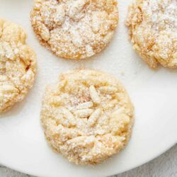Butter almond cookies with powdered sugar and sliced almonds on white plate.