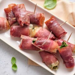 Mini prosciutto-wrapped cheese and basil appetizers on white serving platter.