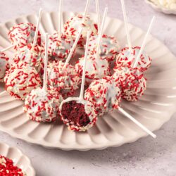 Cream cheese stuffed red velvet cake pops with white chocolate coating and red sprinkles.