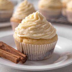 Cream cheese frosting cupcake with cinnamon sticks on white plate, cozy baking image.
