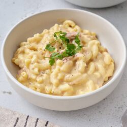 Creamy macaroni and cheese with herbs in a white bowl, classic comfort food recipe.