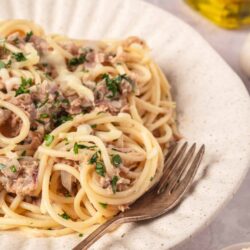 Creamy tuna pasta with parsley on a white speckled plate, ready to serve.