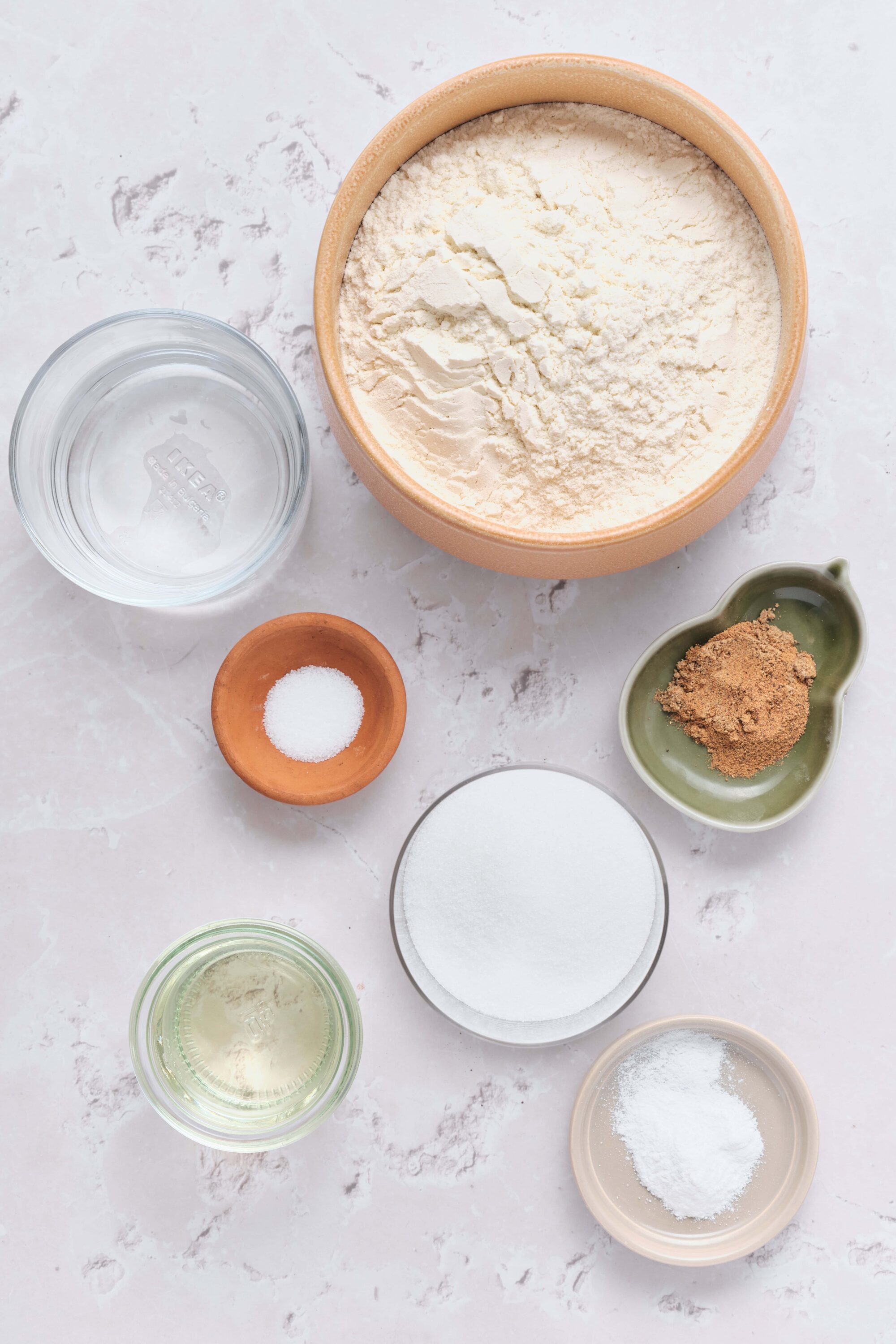 Flour, sugar, baking ingredients arranged on a white surface for baking recipes.
