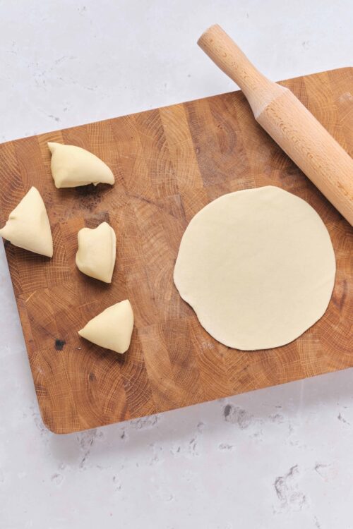 Dough circle and dumplings on wooden cutting board with rolling pin for homemade baked goods.