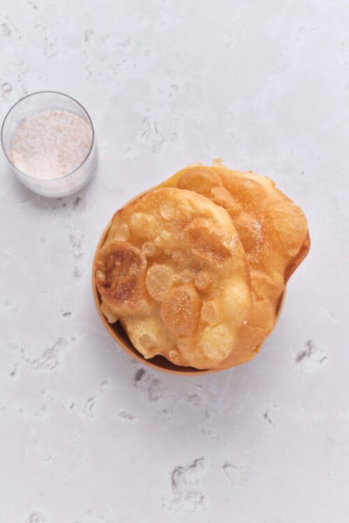 Golden brown fried dough topped with sugar, served in a small bowl.