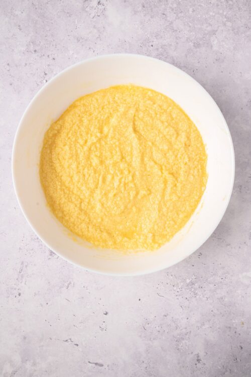 Fluffy yellow cornmeal batter in white bowl, ready for baking.