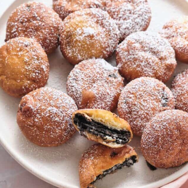 Golden fried Oreos dusted with powdered sugar on a white plate.