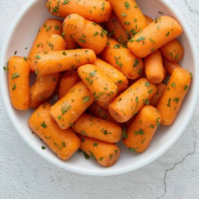 Golden glazed carrots garnished with fresh herbs in a white bowl.