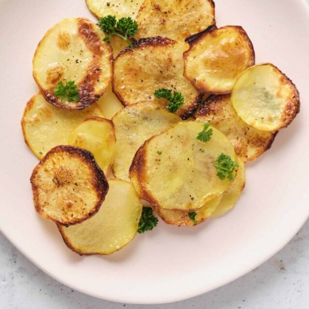 Thinly sliced roasted potatoes garnished with parsley on a white plate.