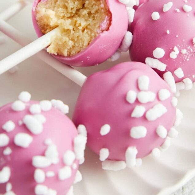Pink cake pops with white sprinkles on a white plate, close-up.