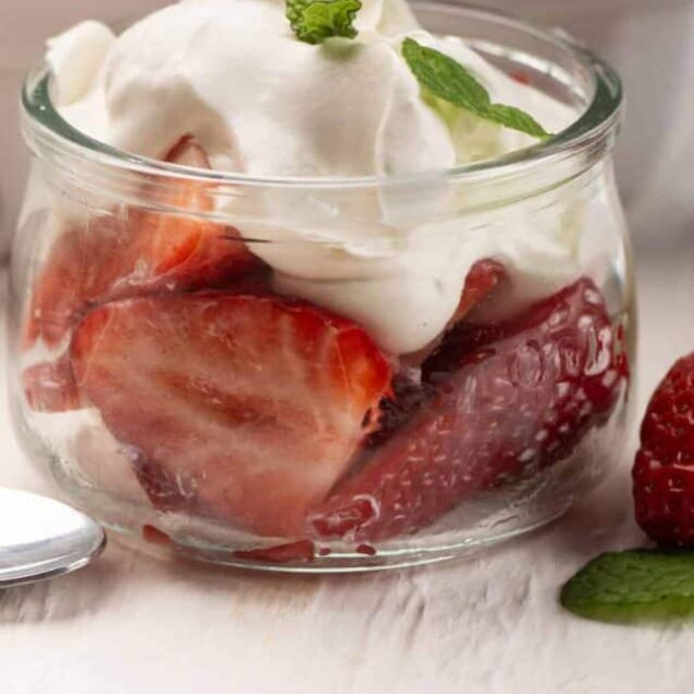 Fresh strawberry shortcake in a glass bowl topped with whipped cream and mint leaves, perfect for summer desserts.