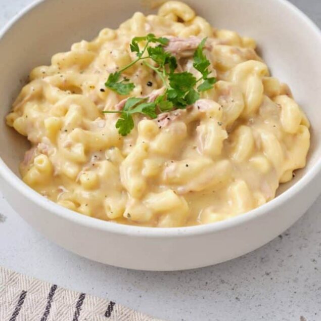Creamy macaroni and cheese served in a white bowl with fresh herbs, comfort food favorite.