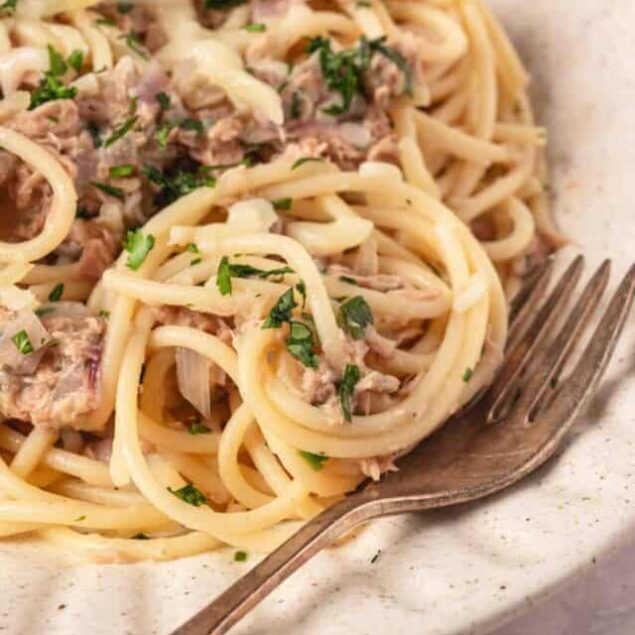 Creamy tuna pasta with parsley on a white speckled plate, ready to serve.