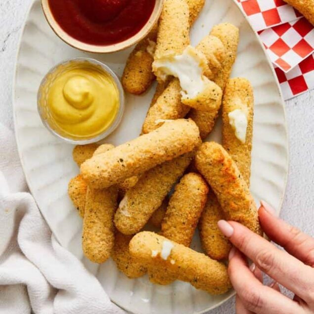 Golden fried mozzarella sticks with creamy dipping sauces on a white plate.