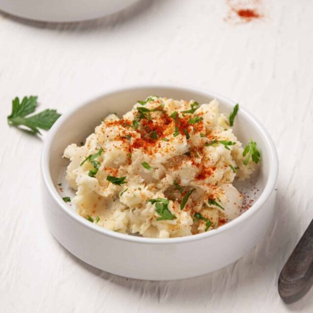 Creamy mashed potatoes with paprika and fresh parsley in a white bowl.