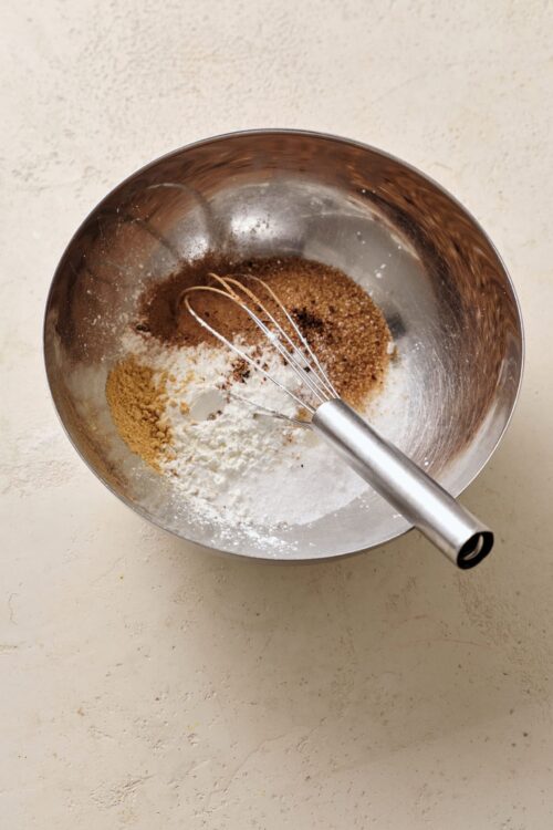 Ground cinnamon, sugar, flour, and cocoa powder in mixing bowl for baking.