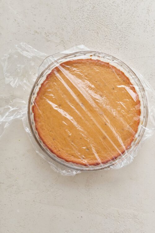 Golden caramel cheesecake wrapped in plastic on a white surface.