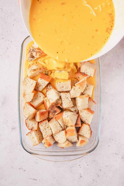 Buttered bread cubes being poured with egg custard mixture for bread pudding recipe.