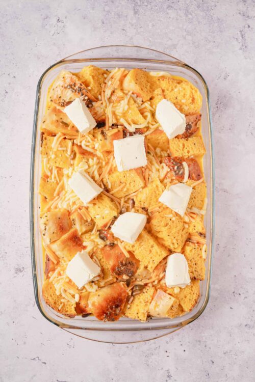 Cheesy bread pudding casserole with bread cubes, cheese, and herbs in a glass baking dish.