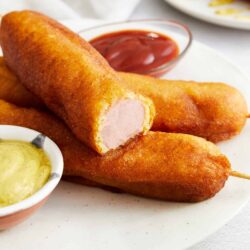 Crunchy fried mozzarella sticks with dipping sauces on a white plate.