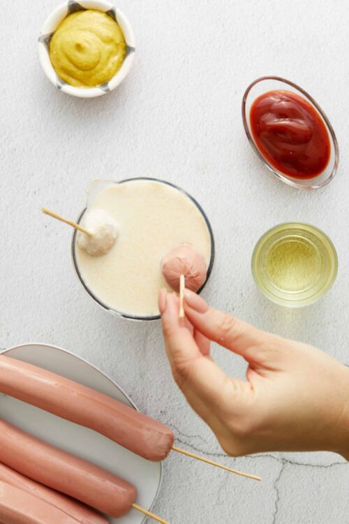 Golden corndog hot dogs with batter on skewers ready to be baked or fried.