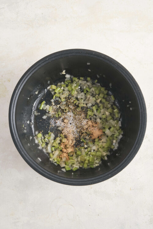 Chopped celery and spices sautéing in a black skillet for flavorful cooking.