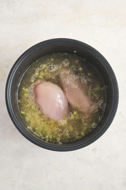 Poached chicken breasts in broth with herbs and green onions, ready for a flavorful recipe.