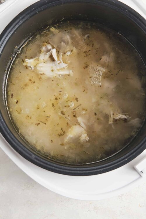 Tender shredded chicken cooking in a flavorful broth in a slow cooker. Perfect for soups, stews, and meal prep.