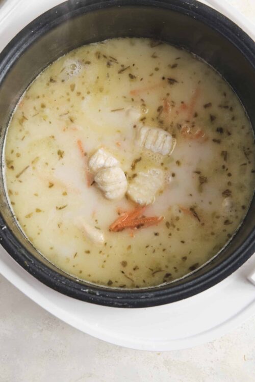 Creamy chicken and vegetable soup cooking in a slow cooker with herbs and spices.