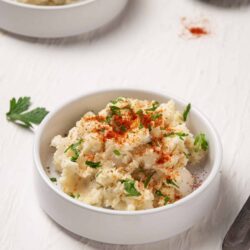 Creamy mashed potatoes with paprika and fresh parsley in a white bowl.