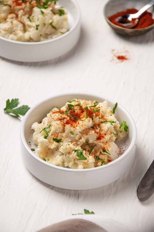 Creamy mashed potatoes with paprika and fresh parsley in a white bowl.