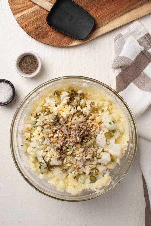 Creamy potato salad with chopped eggs, pickles, and herbs in a glass mixing bowl.