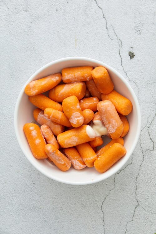 Golden frozen carrots in a white bowl, ready for cooking or roasting.