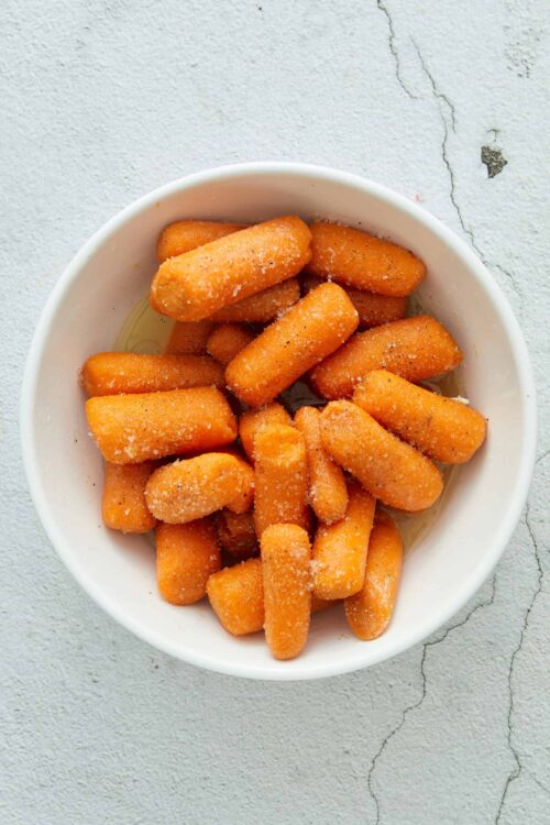 Crispy fried mozzarella sticks in a white bowl with salt and pepper seasoning.