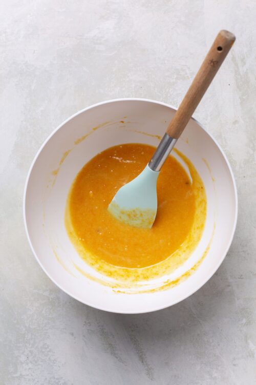 Smooth orange fruit puree in white mixing bowl with spatula, baking, cooking, healthy eating, fresh ingredients, homemade food, dessert ingredients.