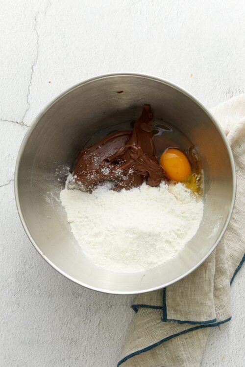 Creamy chocolate frosting ingredients in mixing bowl with egg and flour, ready for baking.