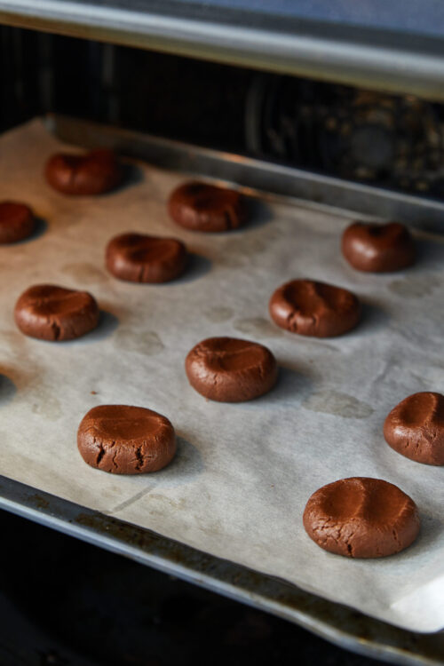 Rich chocolate cookies cooling on parchment paper in a home oven.