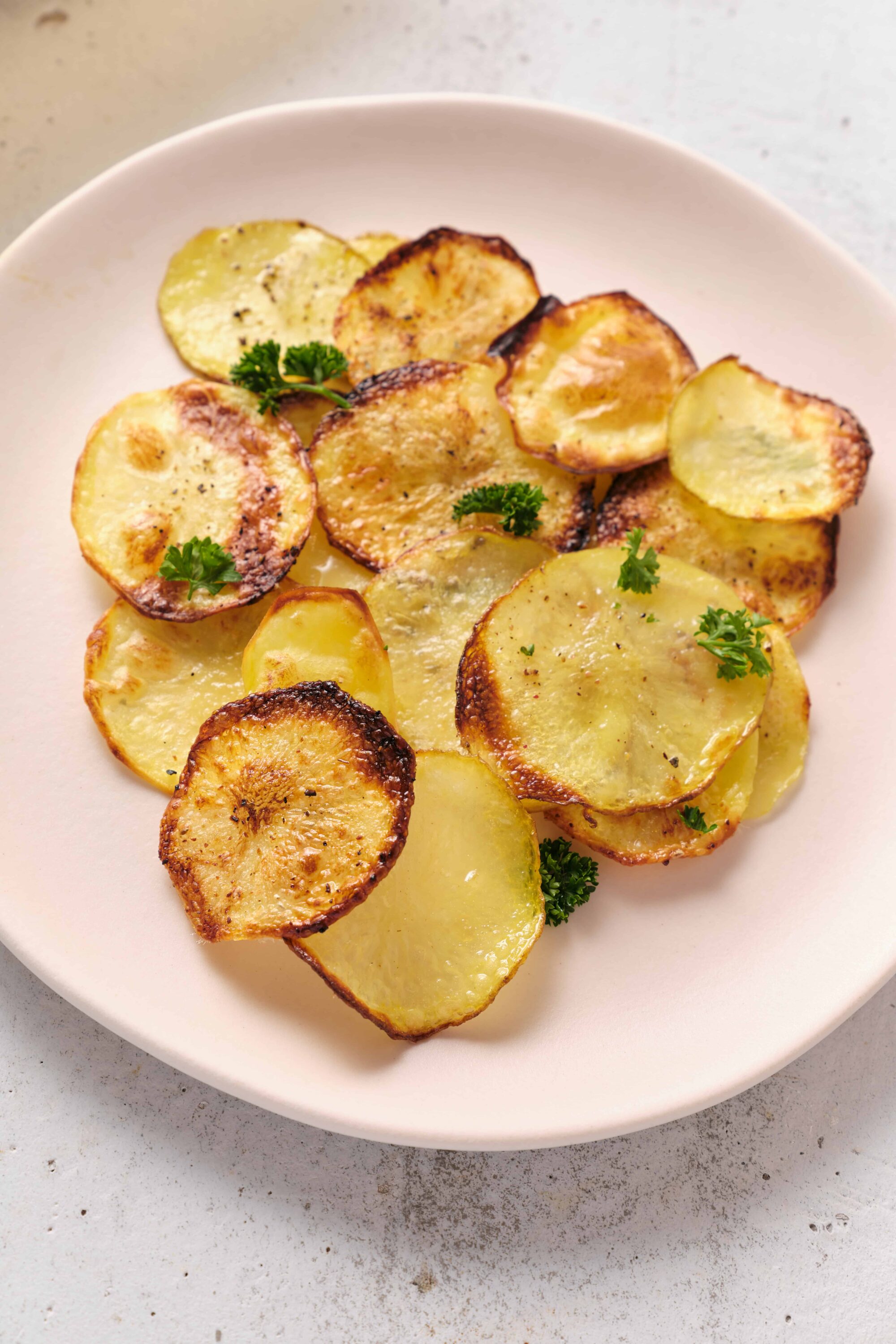 Crunchy roasted potato slices garnished with fresh parsley on a white plate.