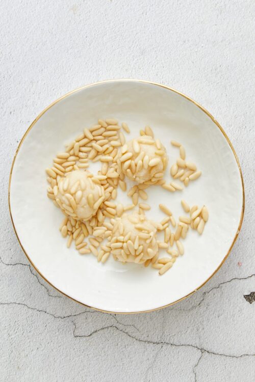 Butter cookie dough truffles with pine nuts on a white plate.