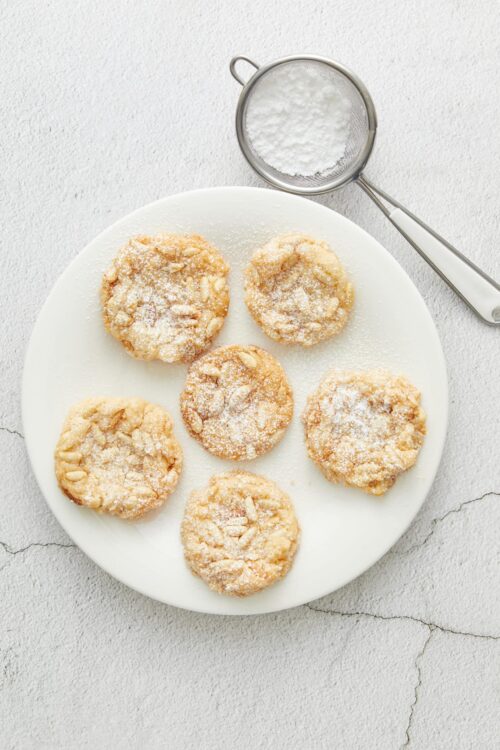Buttery almond cookies with powdered sugar, on a white plate, rustic kitchen style, perfect for holiday pastries.