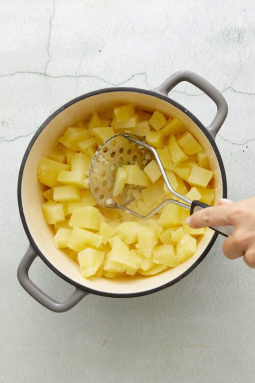 Creamy mashed potatoes in a pot with a masher.